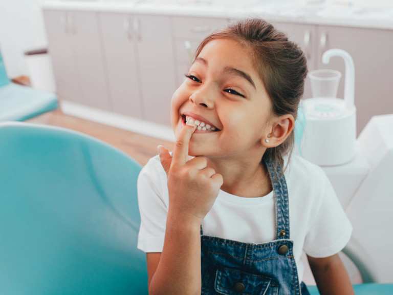 Mixed race little patient showing her perfect toothy smile while sitting dentists chair